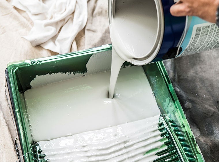 pouring paint into paint tray on top of drop cloth